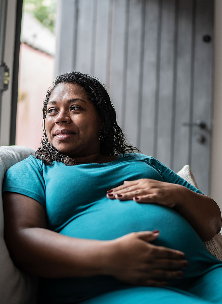 A pregnant Black woman sits on a couch and holds her baby bump
